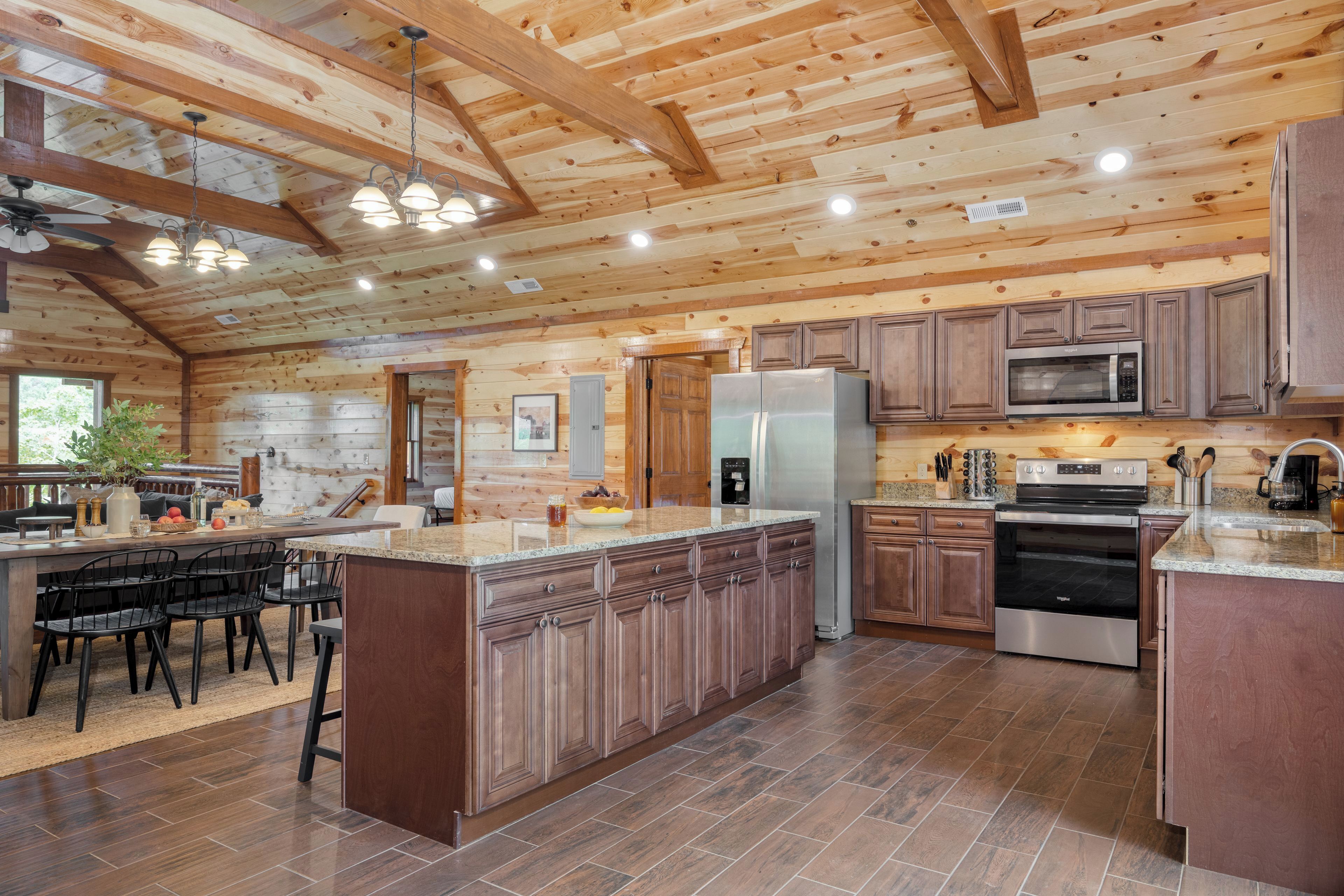 Una cocina amplia con vigas de madera, una isla central, electrodomésticos de acero inoxidable y un comedor con sillas.