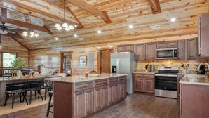 A spacious kitchen with wooden beams, a central island, stainless steel appliances, and a dining area with chairs. - Ridge View by Avantstay15mins From Pigeon Forge w/ Pavilion, Indoor Pool & Hot Tub! (Sevierville)
