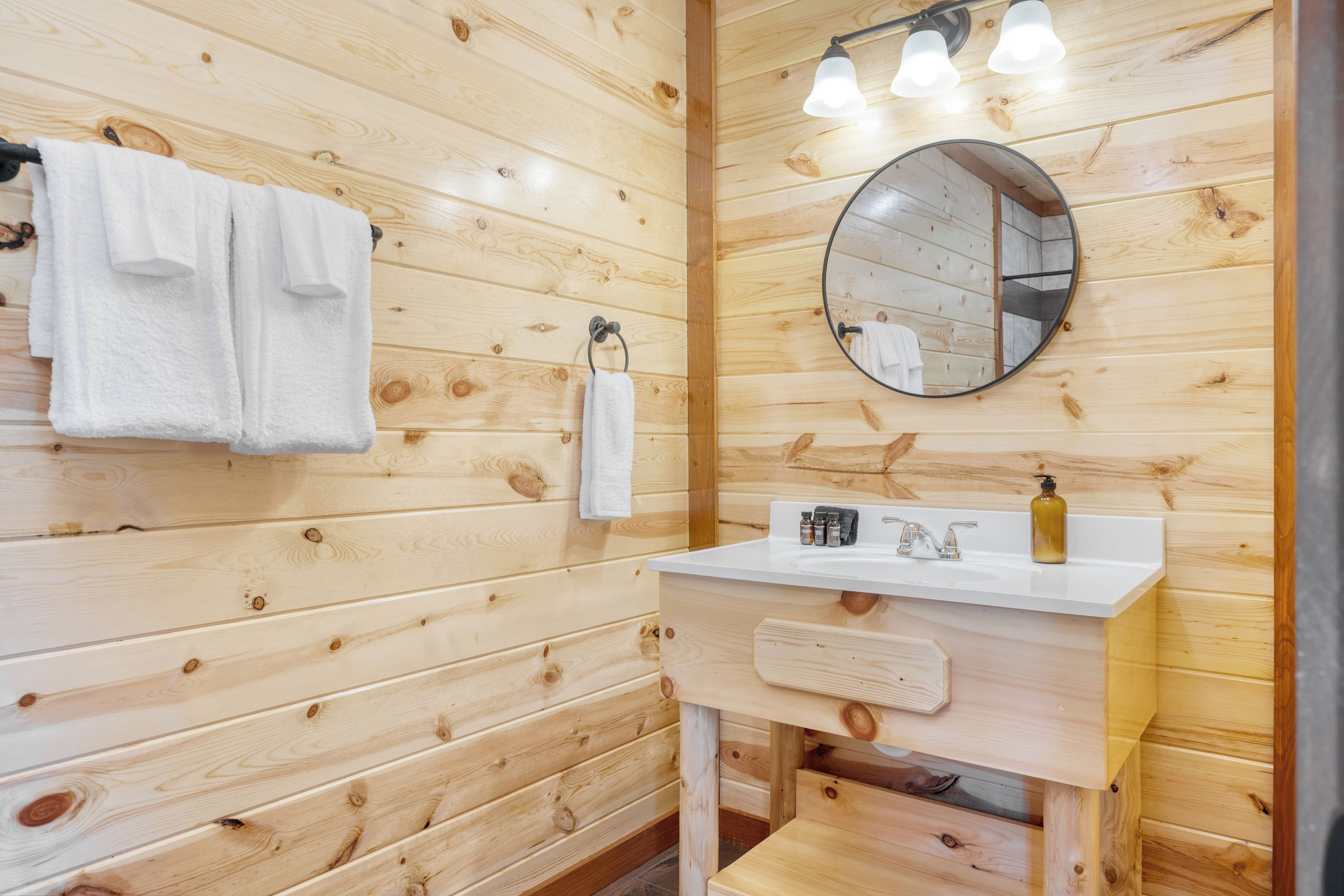 Een badkamer met houten lambrisering, een wit wastafelmeubel, een spiegel en twee handdoeken aan de muur.
