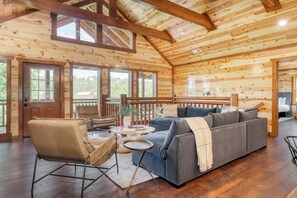 A wooden cabin interior with a sofa, chairs, a small table, and a balcony.