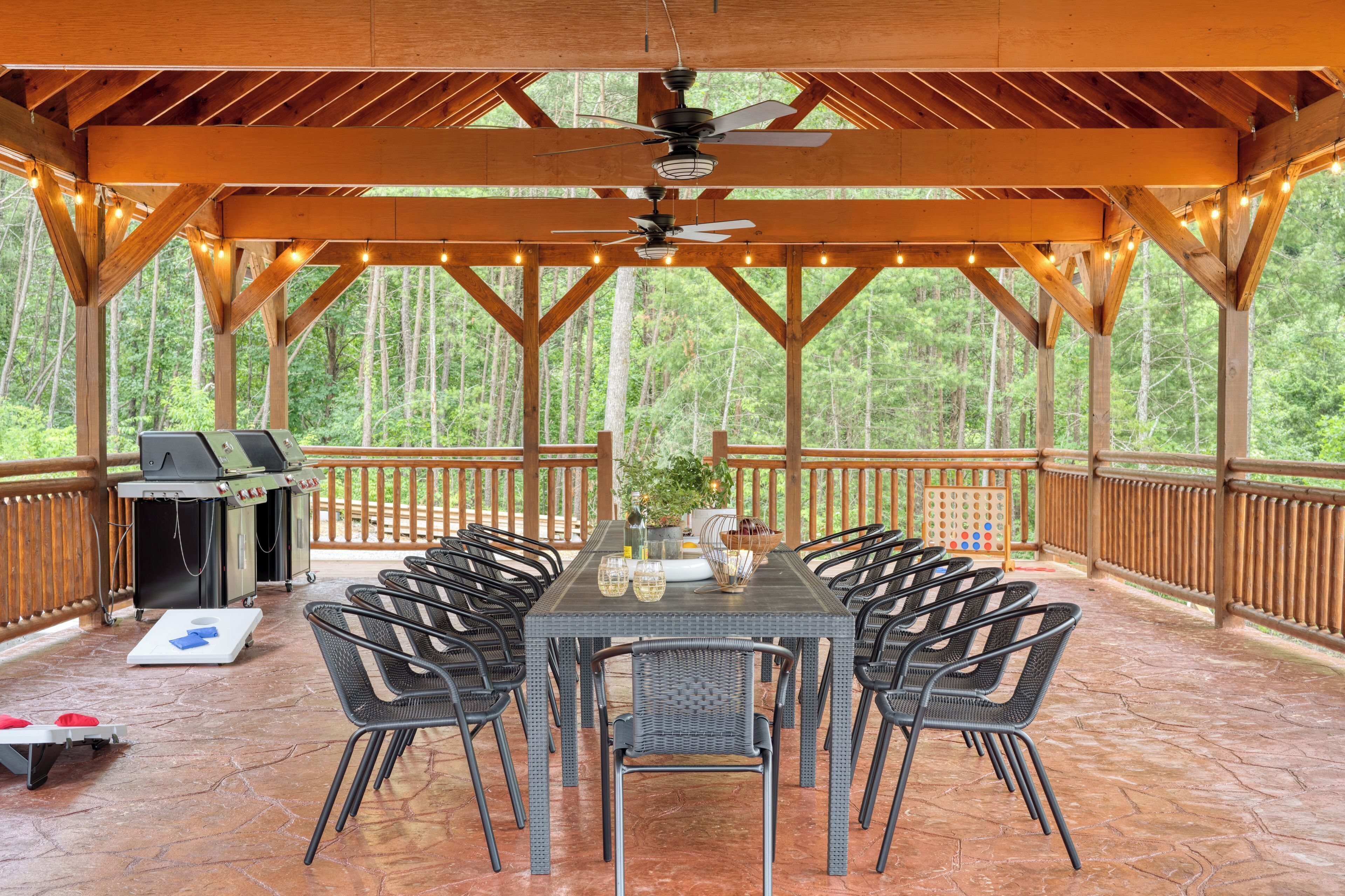 An outdoor covered patio with a table and chairs, a grill, and a view of the forest.