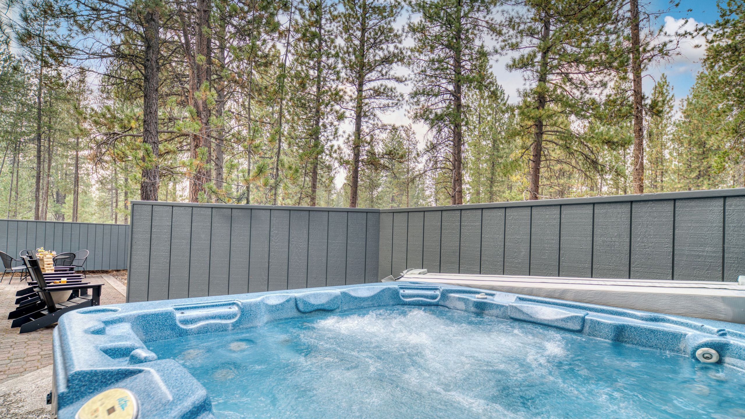 A hot tub surrounded by a wooden deck, with a view of tall pine trees in the background.