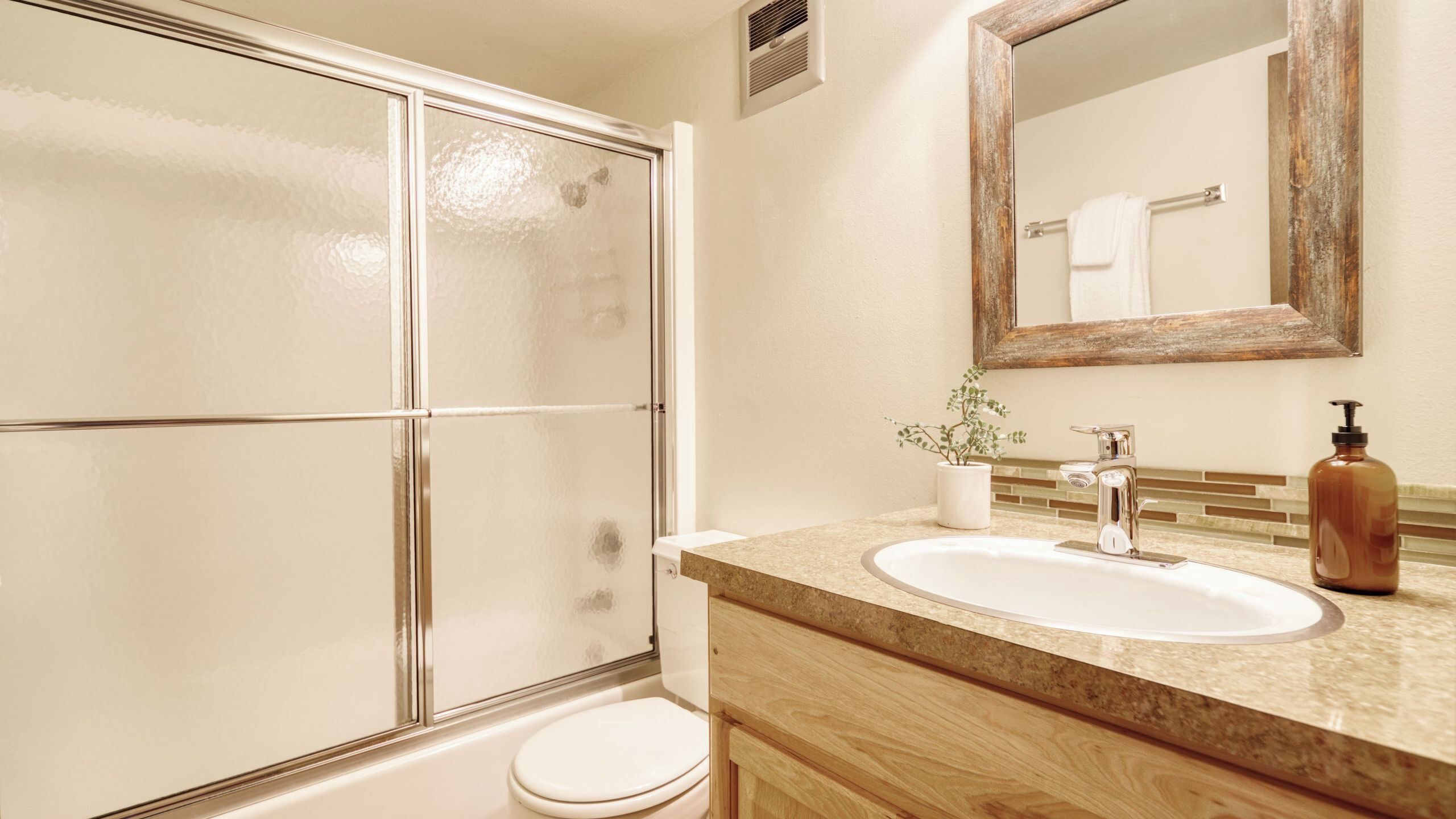 A bathroom with a glass shower enclosure, a white toilet, a sink with a wooden vanity, and a mirror above the sink.