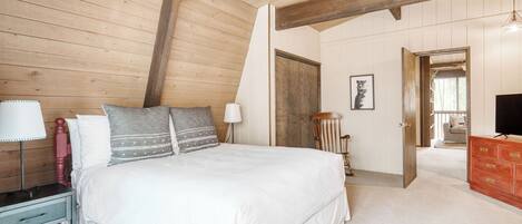 A bedroom with a wooden ceiling, a bed with white bedding, a wooden chair, a dresser, and a television.