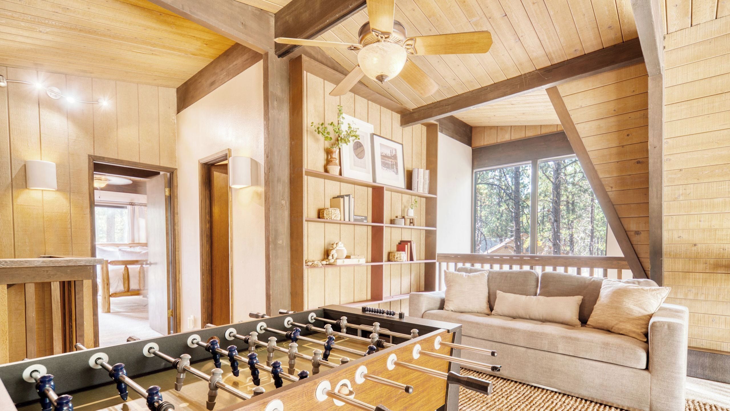 A cozy room with a foosball table, a sofa, a bookshelf, and a ceiling fan.