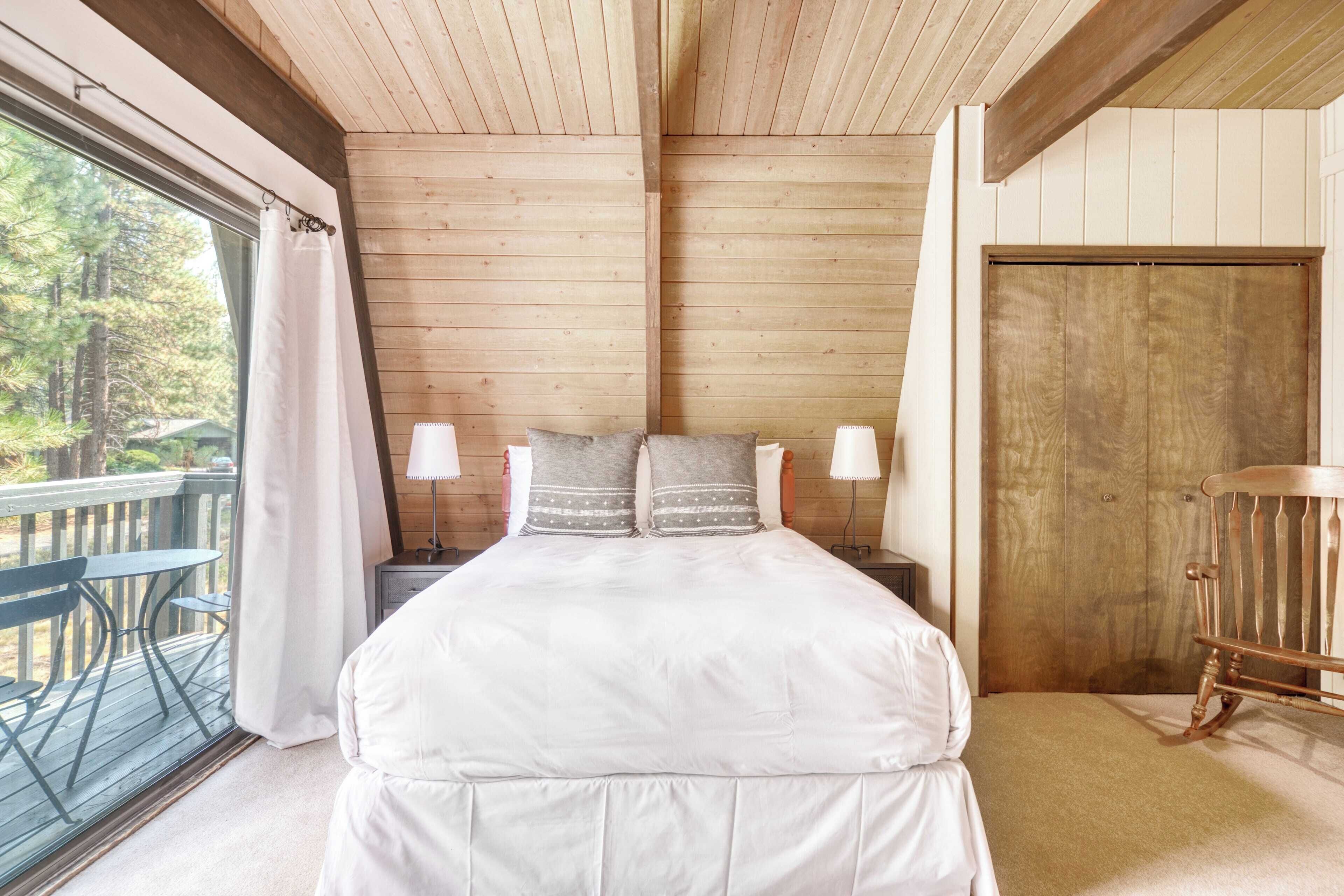 Une chambre à coucher dans une cabane en bois, avec un lit, deux lampes de chevet, une porte en bois et une vue sur l’extérieur.
