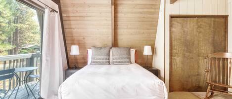 Une chambre à coucher dans une cabane en bois, avec un lit, deux lampes de chevet, une porte en bois et une vue sur l’extérieur.