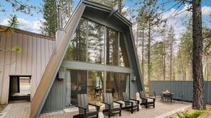A modern house with a sloped roof, large windows, and a patio with outdoor seating. - Alder by Avantstay Hot Tub + Fireplace + Foosball Loft + Patio Grill Walk to Sunriver Village + Trails + Mt. Bachelor 30 Min (Bend)