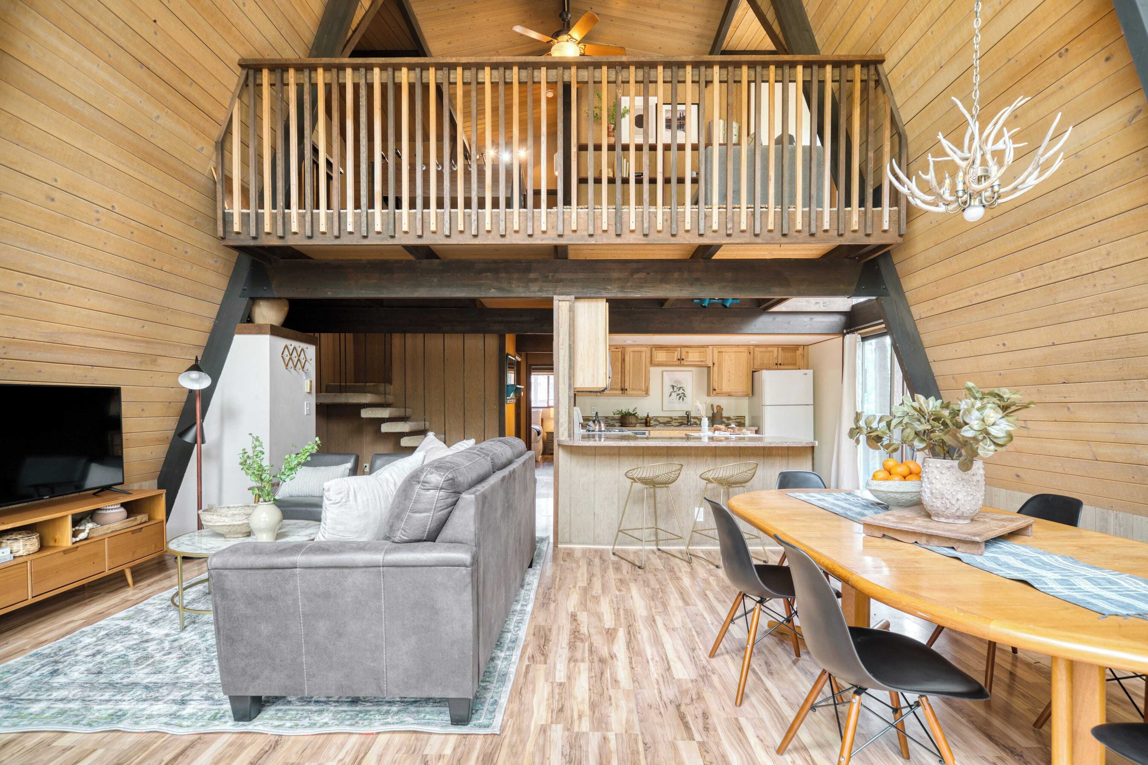 A spacious living area with a grey sofa, wooden flooring, a dining table with chairs, a kitchen area, and a balcony with a railing.