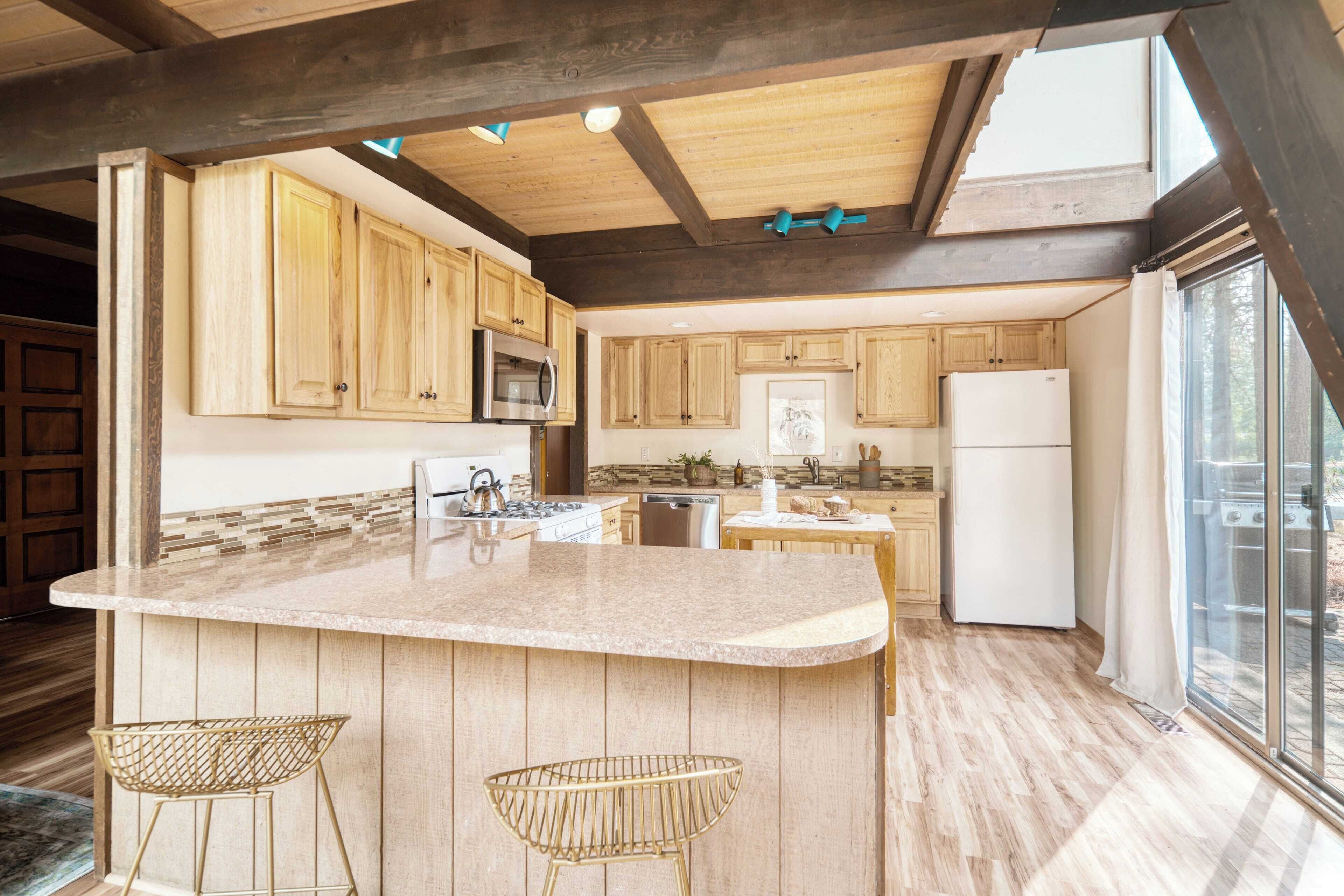 A spacious kitchen with wooden cabinets, a granite countertop, and two bar stools.