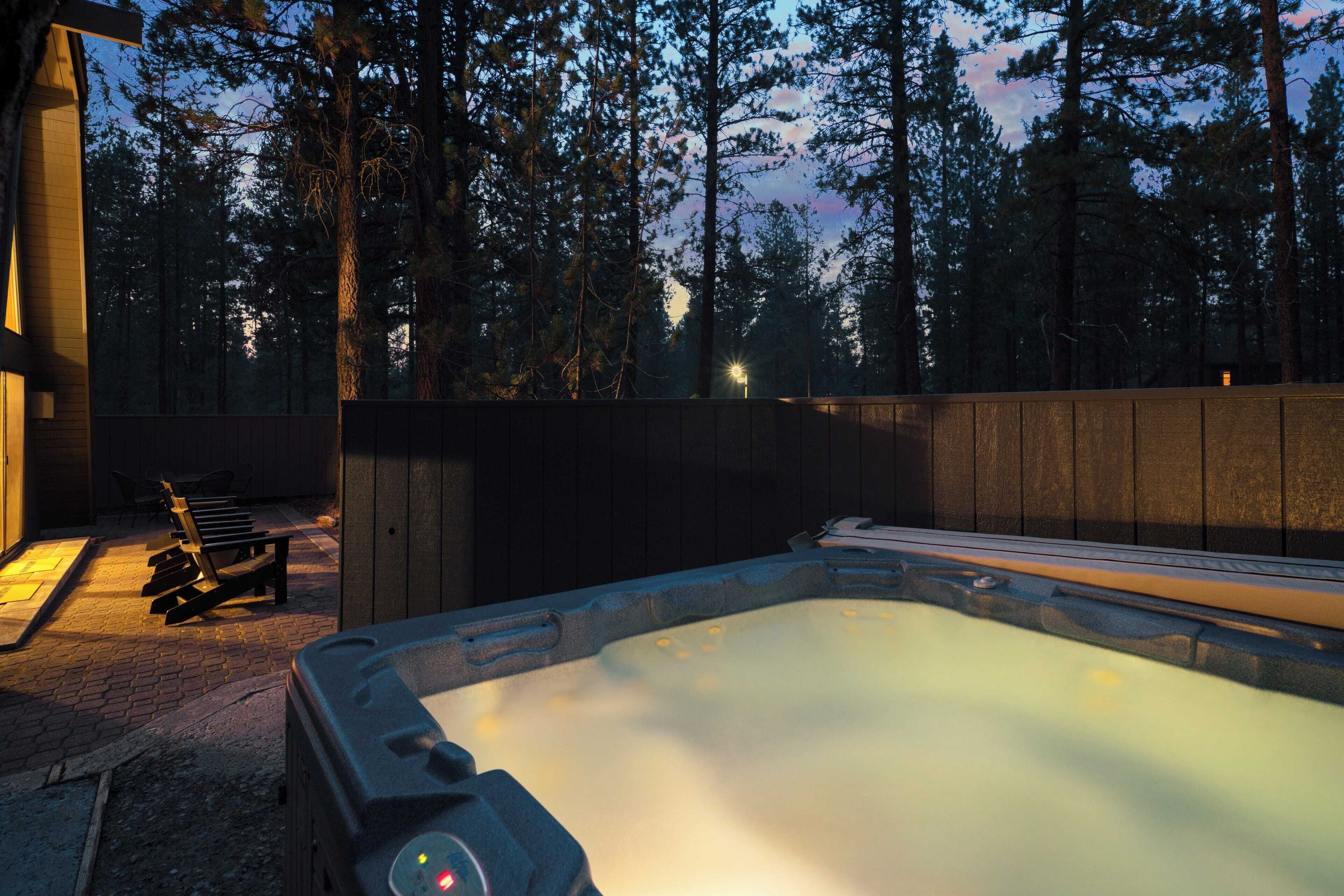A hot tub in a wooded area with a bench and a wooden fence.