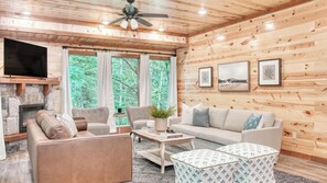 A cozy cabin interior with a stone fireplace, a sofa, a coffee table, and a television.