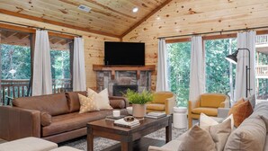 A wooden cabin interior with a stone fireplace, leather sofas, a coffee table, and large windows. - Bluestem & Bluebell by Avantstay Incredible Views w/ Large Balcony & Indoor Pool! (Sevierville)