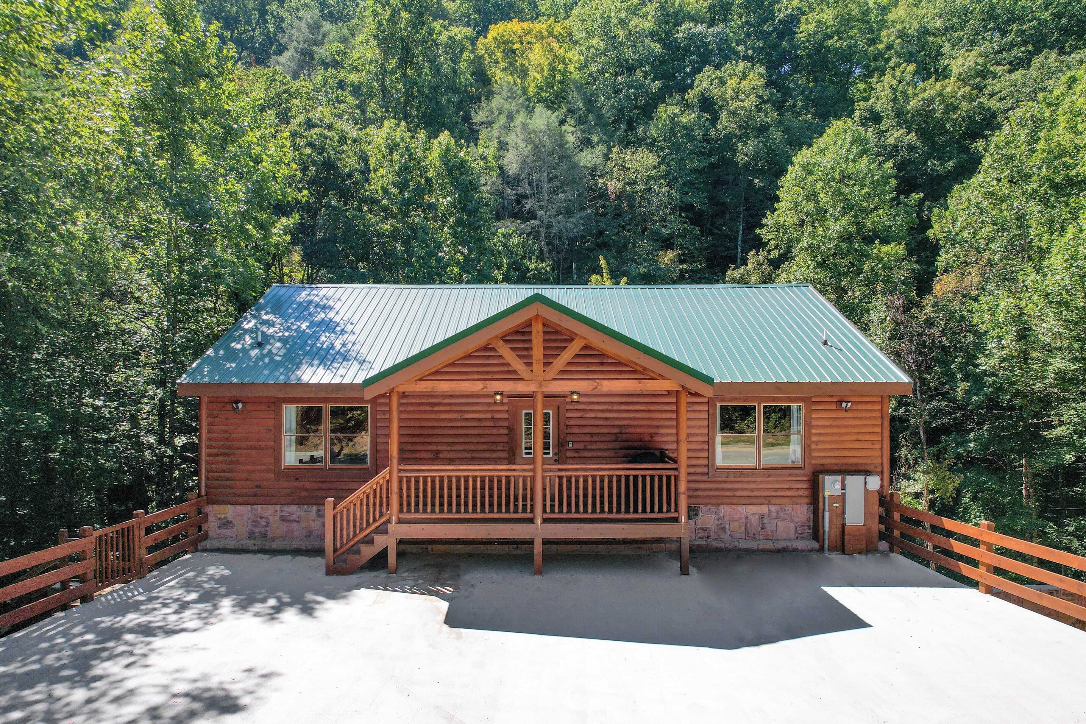 Une cabane en bois avec un toit vert, une véranda et un espace clôturé.