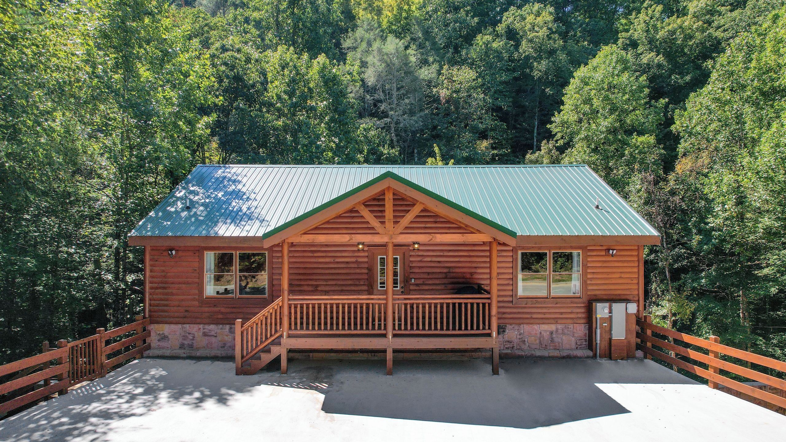 A wooden cabin with a porch, surrounded by forest.