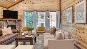 A cozy log cabin interior with a stone fireplace, leather sofas, a coffee table, and a television. - Bluestem & Bluebell by Avantstay Incredible Views w/ Large Balcony & Indoor Pool! (Sevierville)