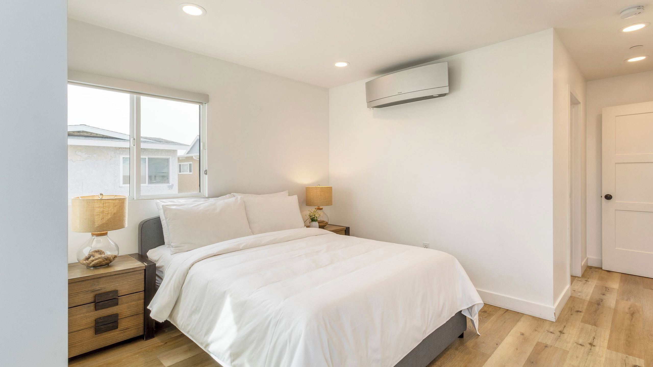 Une chambre à coucher comprenant un lit, des tables de chevet, une fenêtre et un appareil de climatisation.