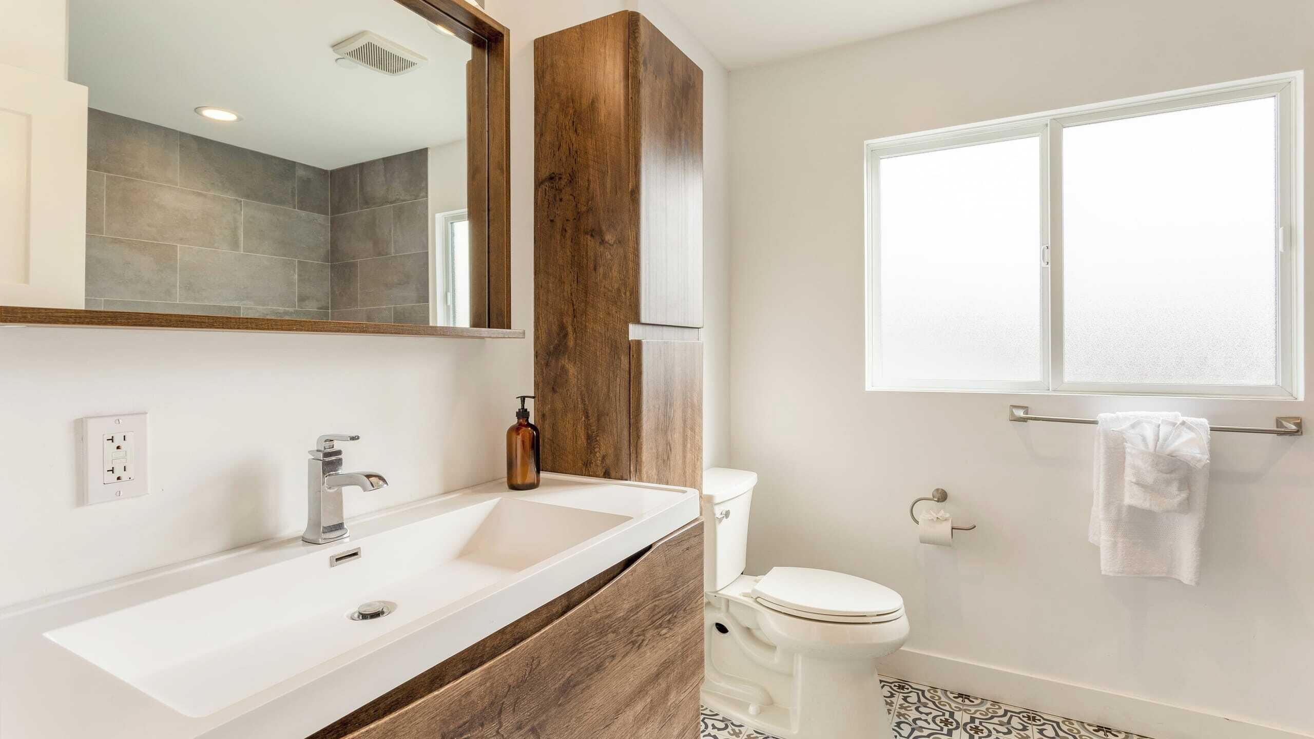 A bathroom with a double sink, a toilet, a mirror, and a window.