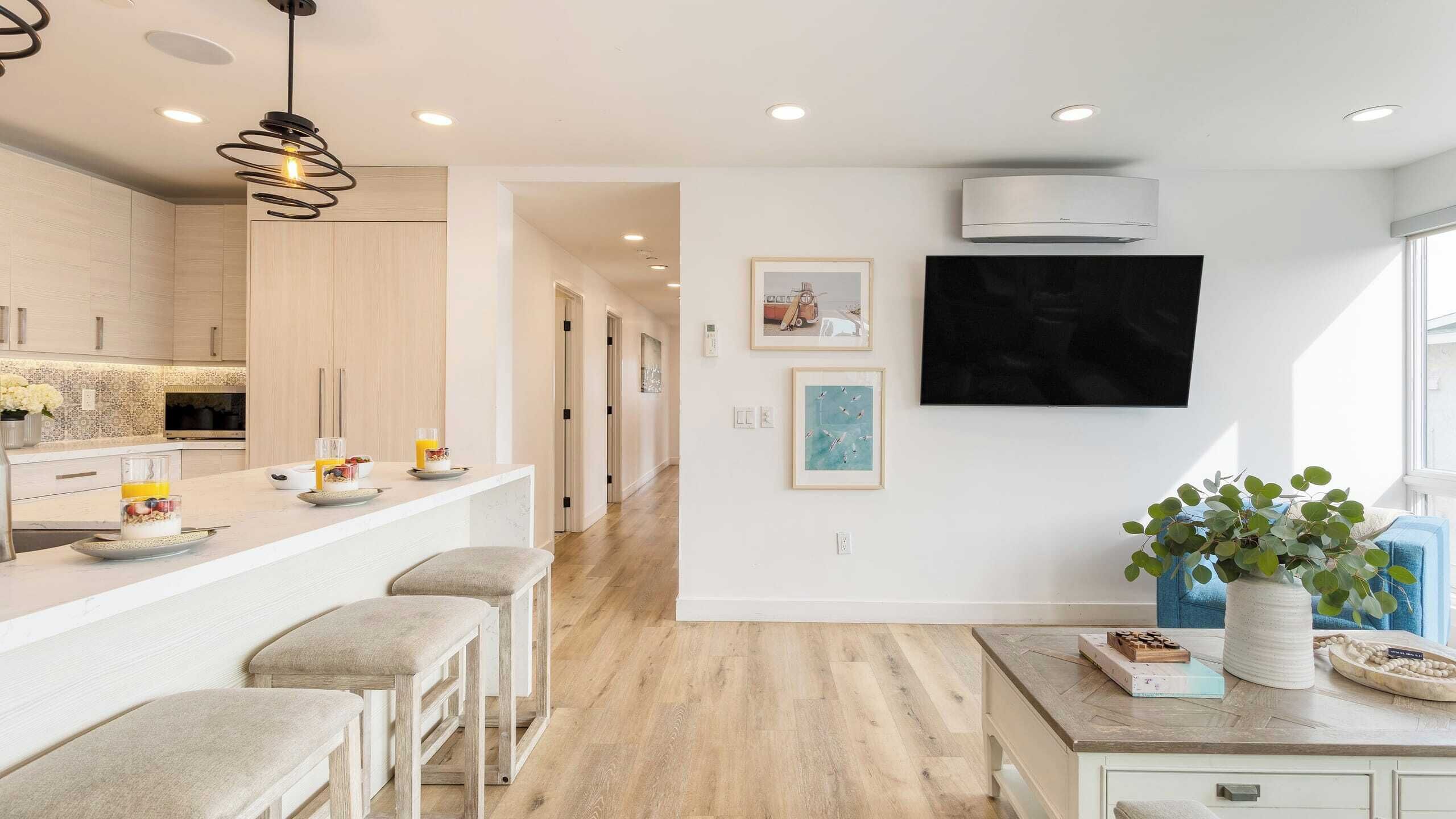 A modern kitchen with a bar area, wooden flooring, and a mounted flat-screen TV.