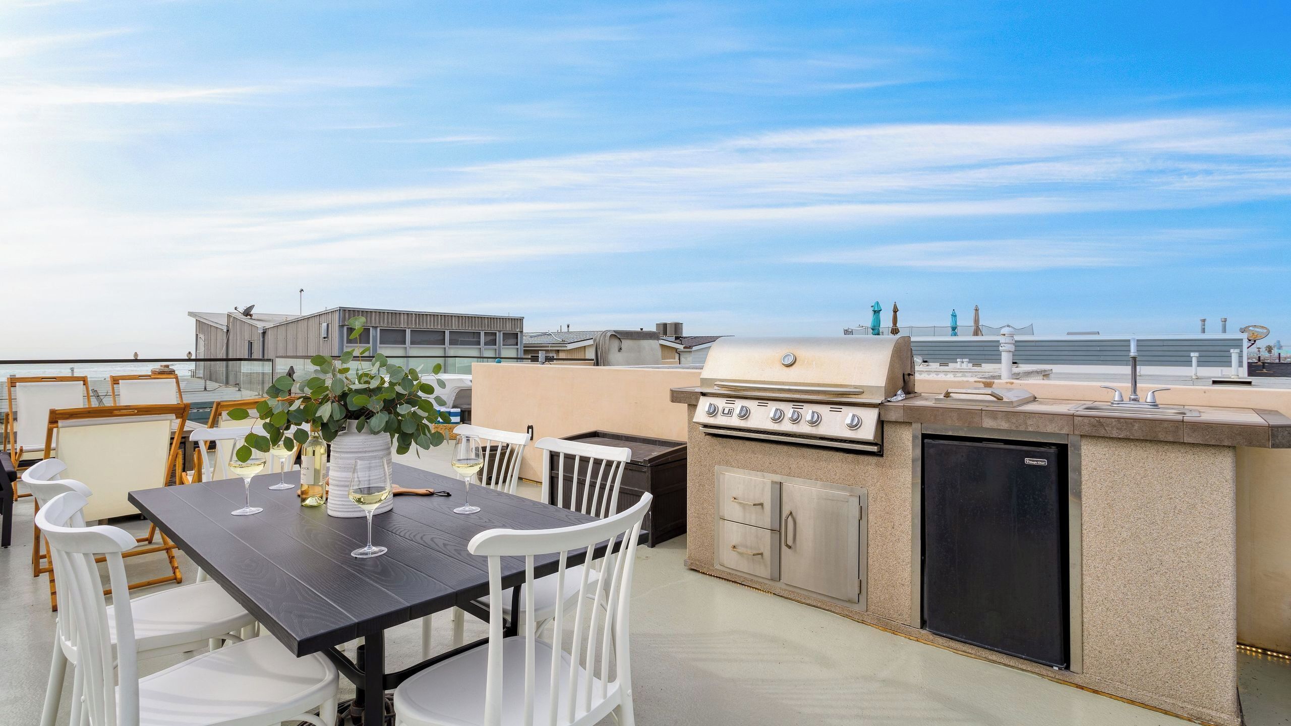 Un patio al aire libre con una mesa preparada para comer, una parrilla y vistas al mar.