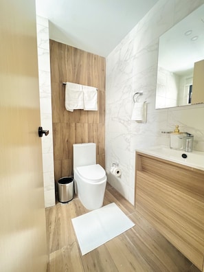 Een moderne badkamer met een houten wastafelmeubel, een toilet en een marmeren spatwand.
