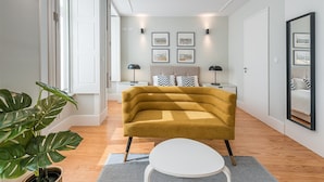 A modern living room with a mustard-colored sofa, a white coffee table, and a large potted plant. - Sunny getaway in Rua do Bonjardim (Porto)