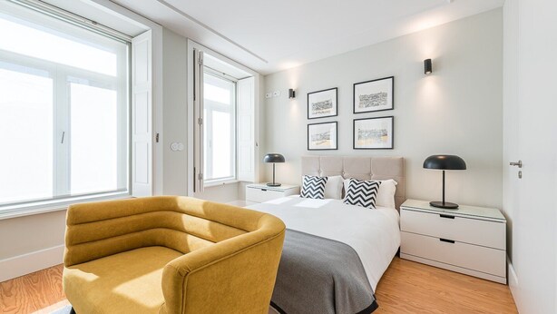 A modern bedroom with a large bed, bedside tables, a chair, and artwork on the wall. - Sunny getaway in Rua do Bonjardim (Porto)