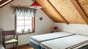 A bedroom with a sloped ceiling, a window with a floral curtain, a bedside table with a lamp, and two mattresses.
