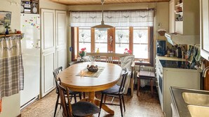 A cozy kitchen with a wooden dining table, white cabinets, and a window with a view of trees.