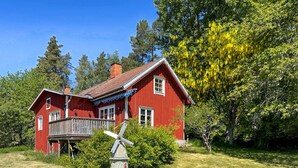 A red wooden house with a balcony, surrounded by greenery and trees.