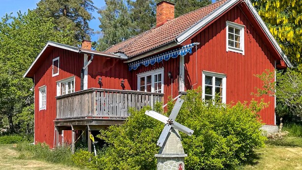A red wooden house with a balcony and a windmill in front.