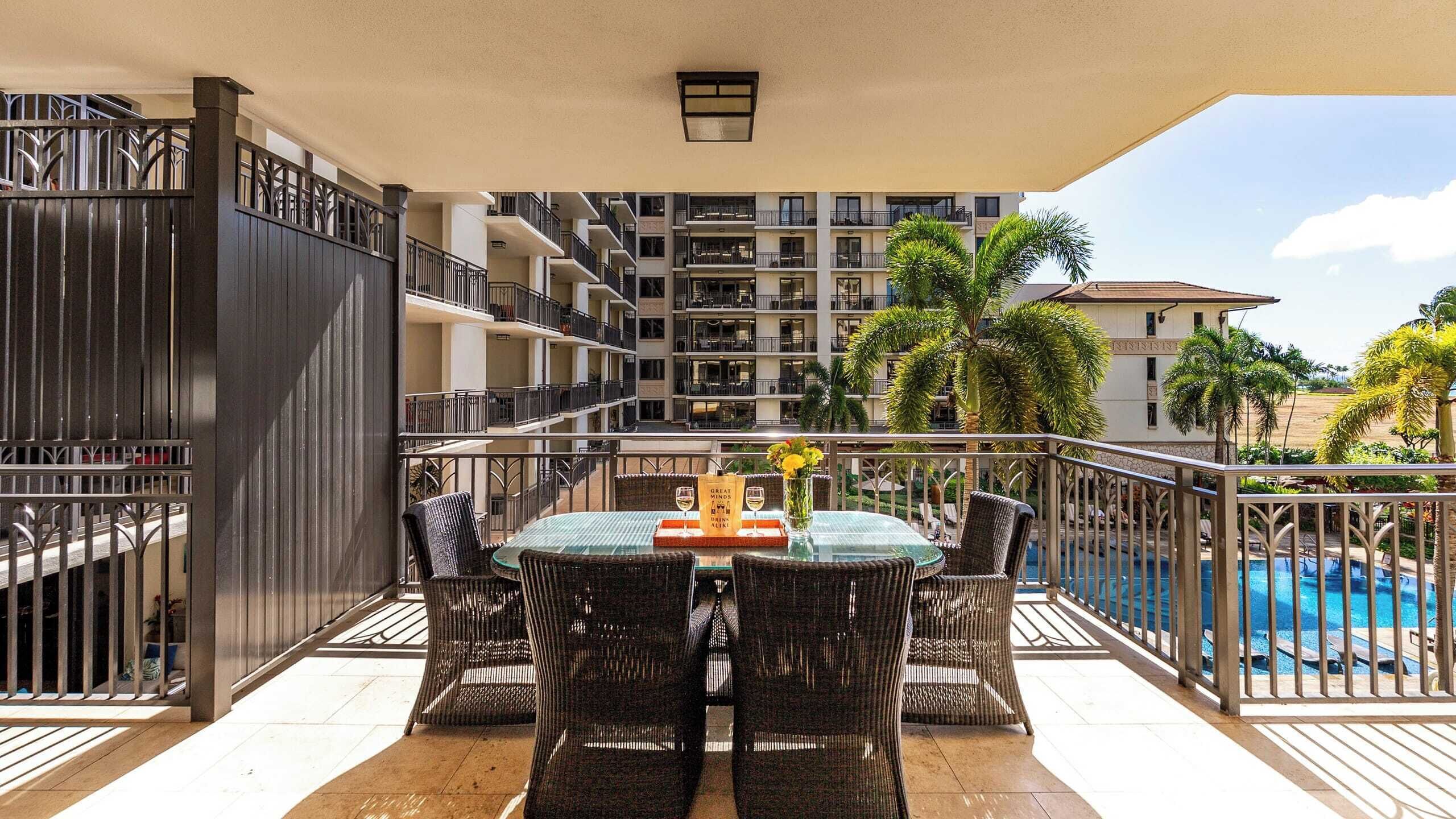 A balcony with wicker furniture, a glass table, and a pool in the background.