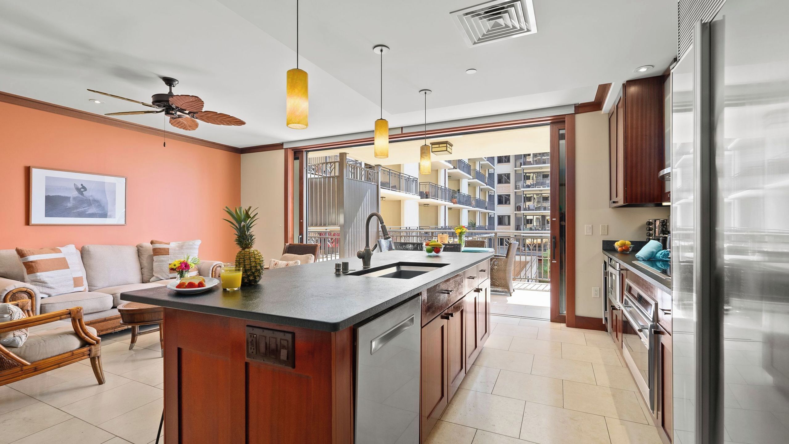 A modern kitchen with a central island, a dining area with a sofa, and a view of a residential building.