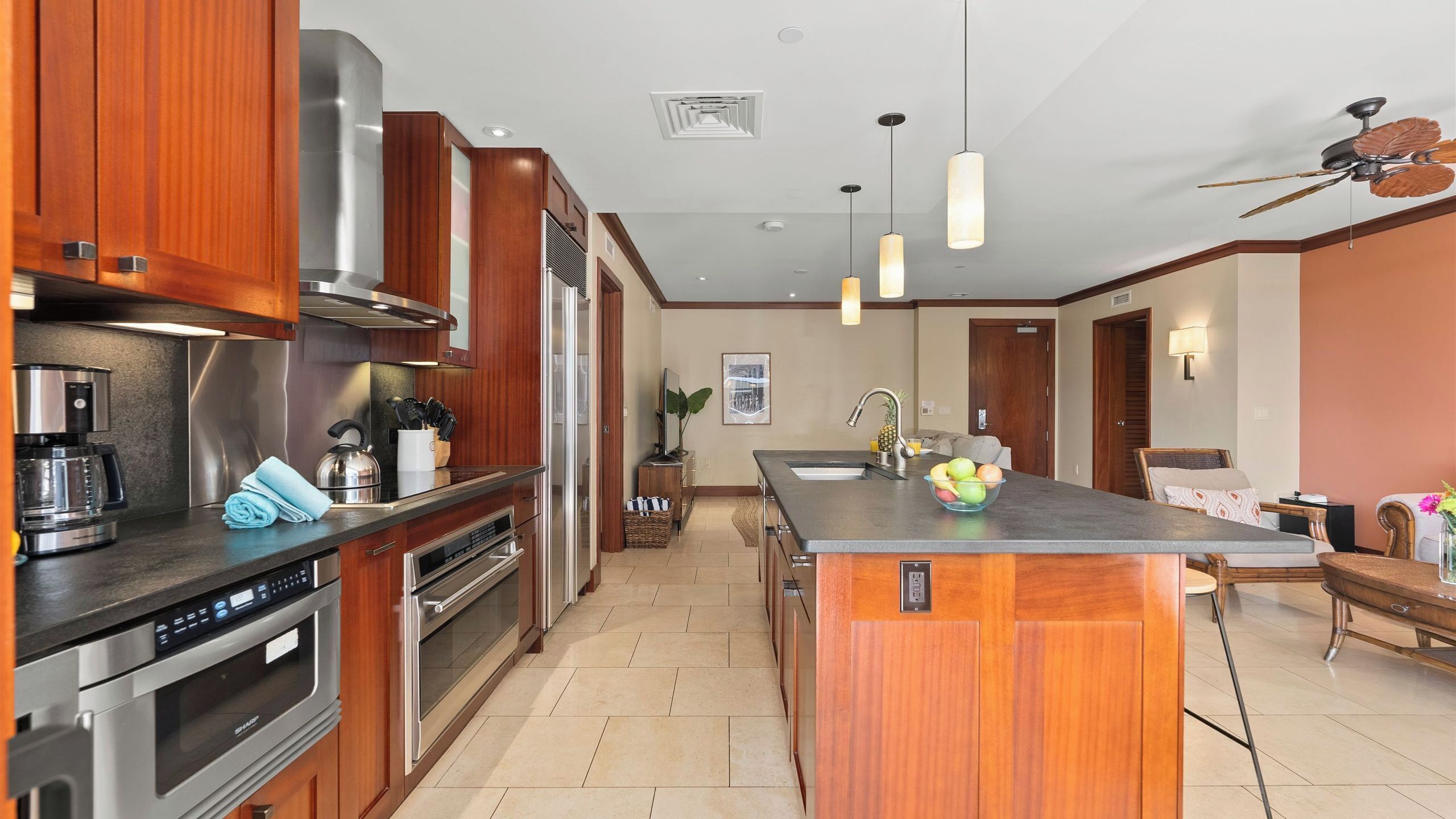 A modern kitchen with stainless steel appliances, wooden cabinets, and a central island with a bowl of fruit.