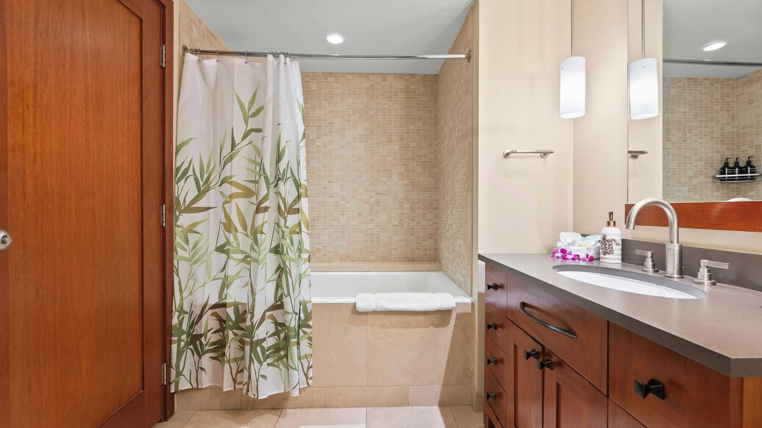 A bathroom with a bamboo shower curtain, a bathtub, a vanity with a sink, and a mirror.