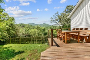 A wooden deck with outdoor furniture, a white building, and a view of green hills. - Penny by Avantstay Weaverville Home w/ Mtn Views (Weaverville)