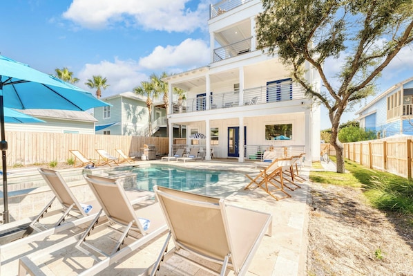 A pool area with lounge chairs and a two-story building with balconies.