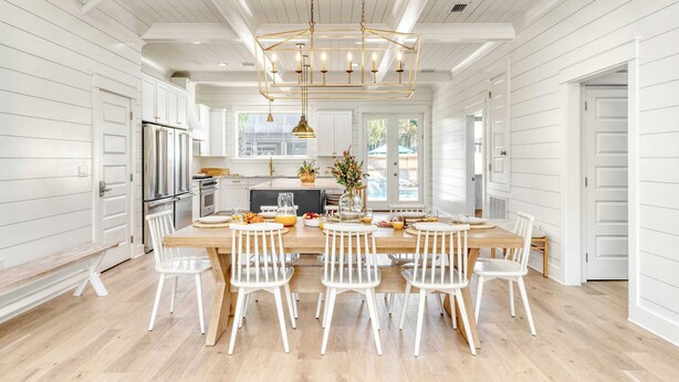 Une cuisine spacieuse avec des meubles blancs, un grand îlot central doté de chaises et un luminaire suspendu.