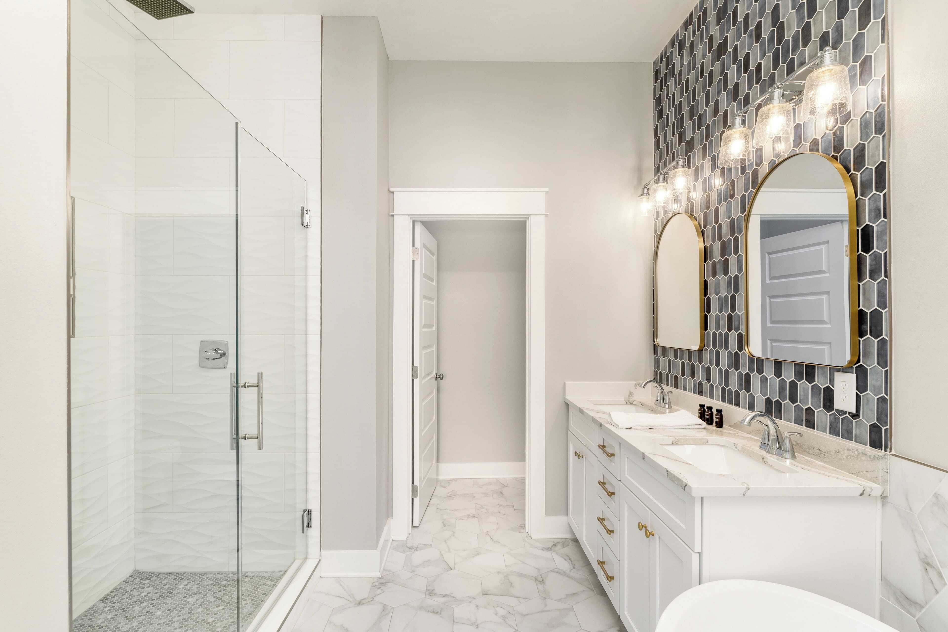 A modern bathroom with a glass shower enclosure, a walk-in closet, and a vanity with two sinks.