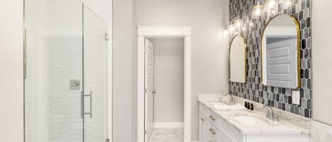 A modern bathroom with a glass shower enclosure, a walk-in closet, and a vanity with two sinks.