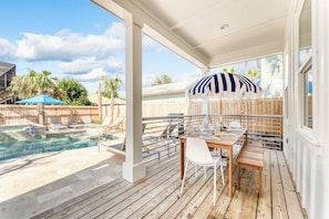 A covered outdoor area with a pool, wooden deck, and a table with chairs.