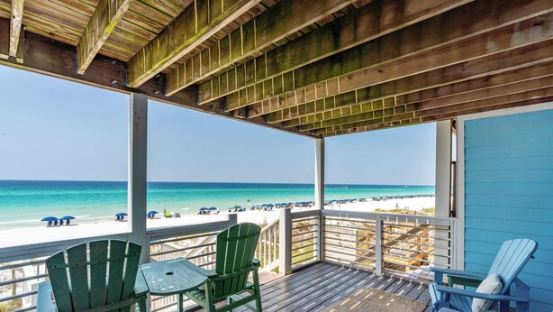 Una terraza de madera con sillas que da a la playa.