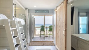 Un pasillo que conduce a un balcón con vistas a la playa, un cartel que dice 'BEACH HOUSE' y una puerta de madera.