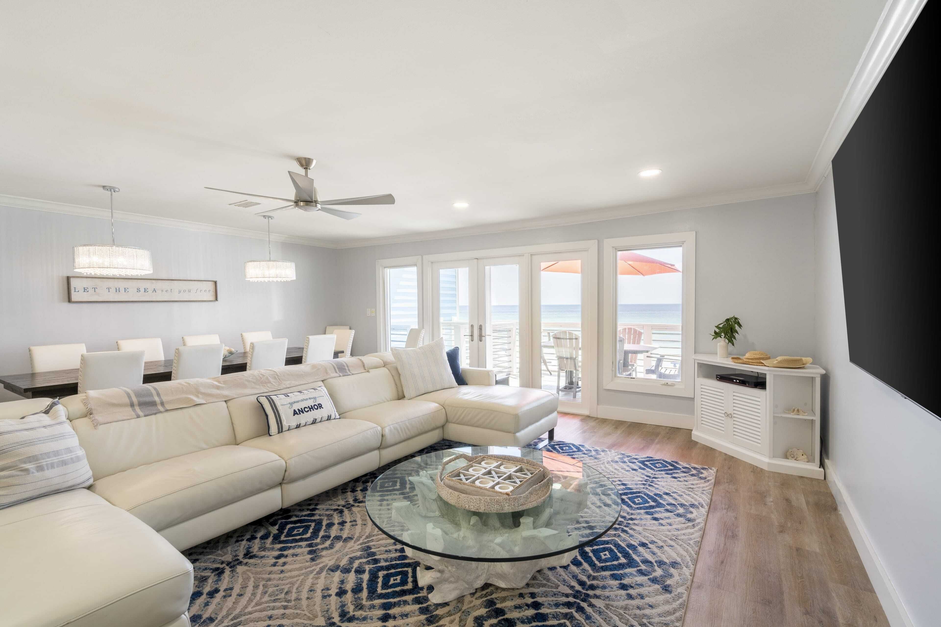 Ein modernes Wohnzimmer mit einer großen Eckcouch, einem Glastisch und Blick auf das Meer durch große Fenster.