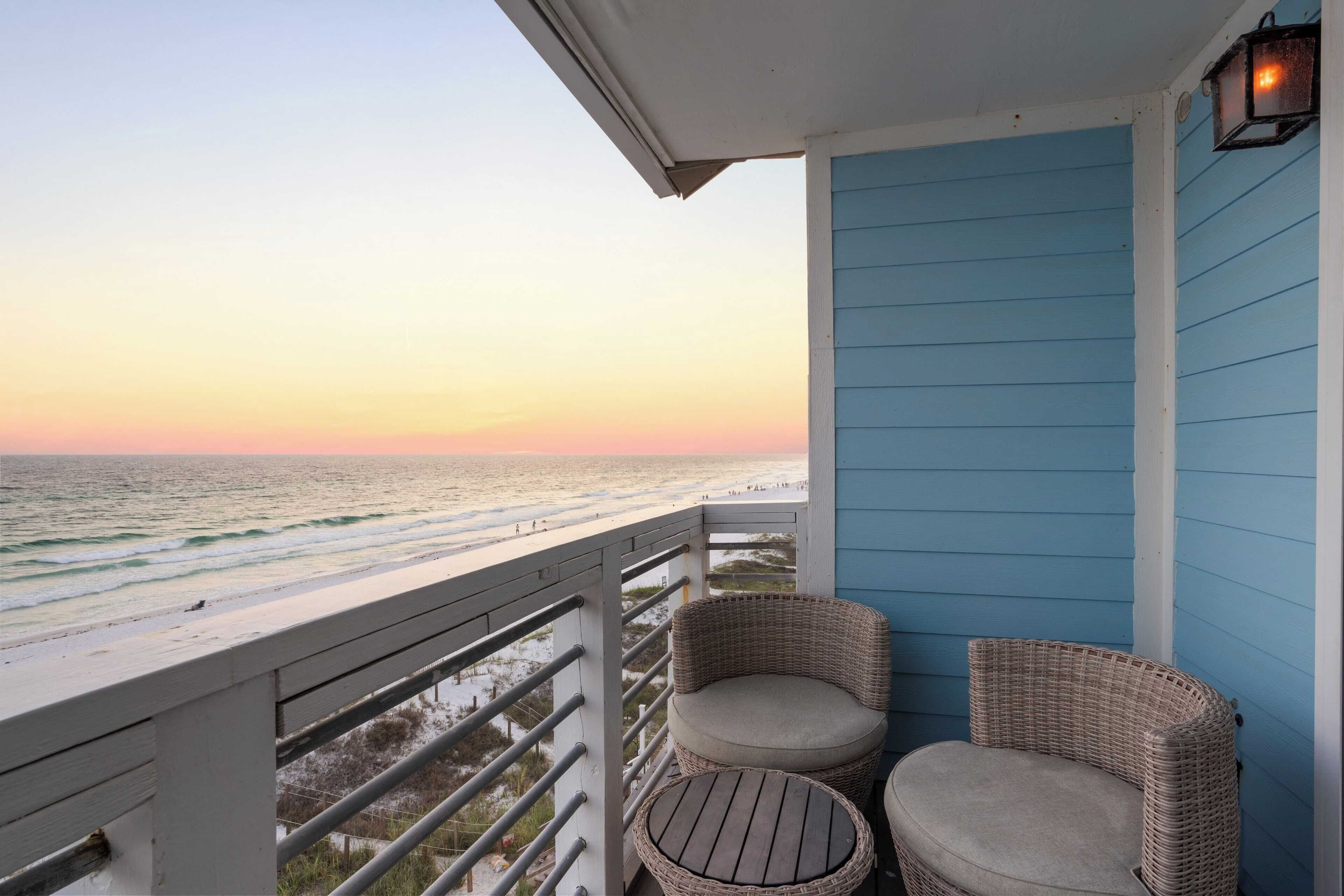 A balcony with wicker furniture and a view of the ocean at sunset.