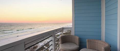 A balcony with wicker furniture and a view of the ocean at sunset.