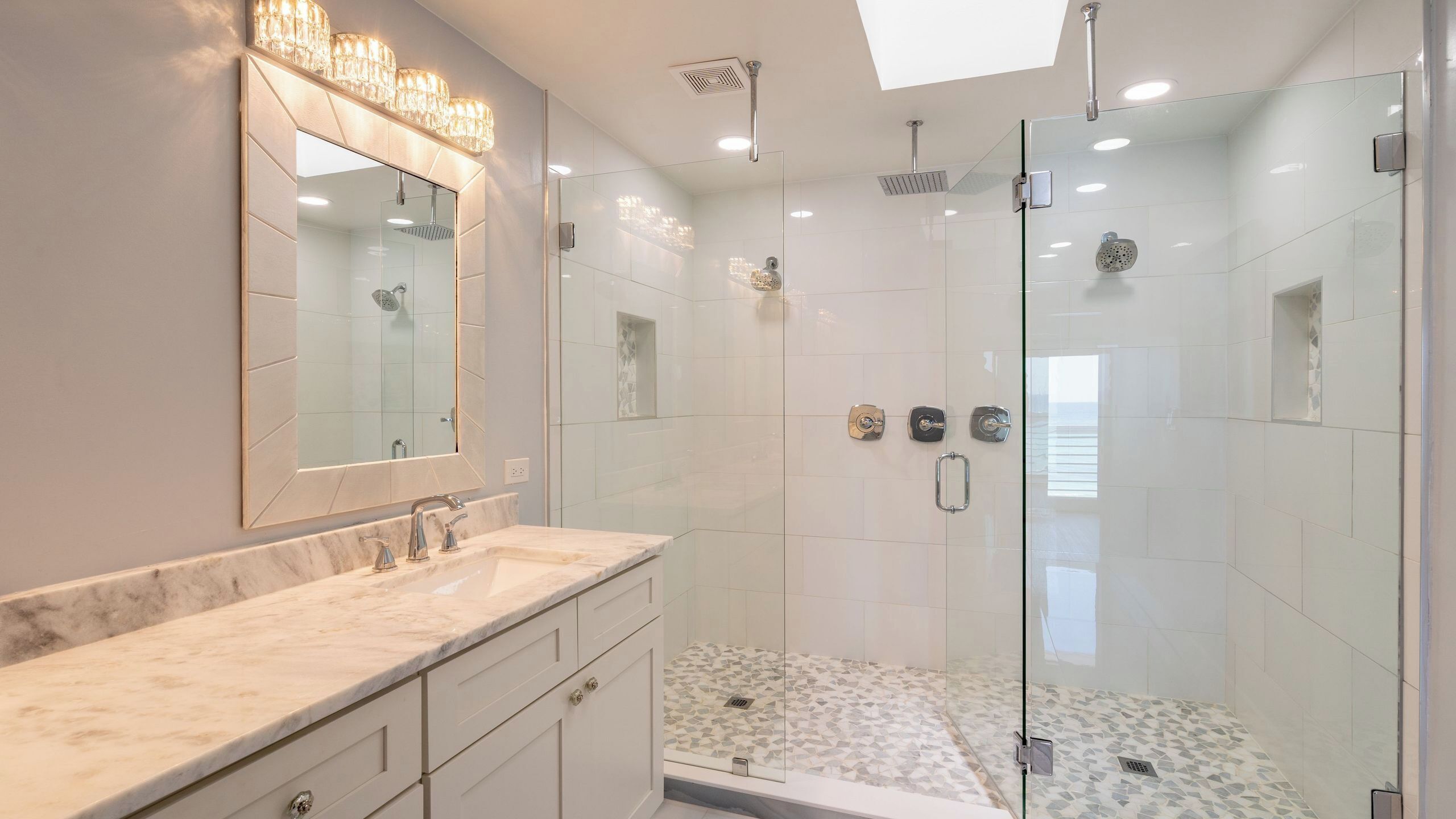 A modern bathroom with a glass-enclosed shower, a marble vanity, and a large mirror.