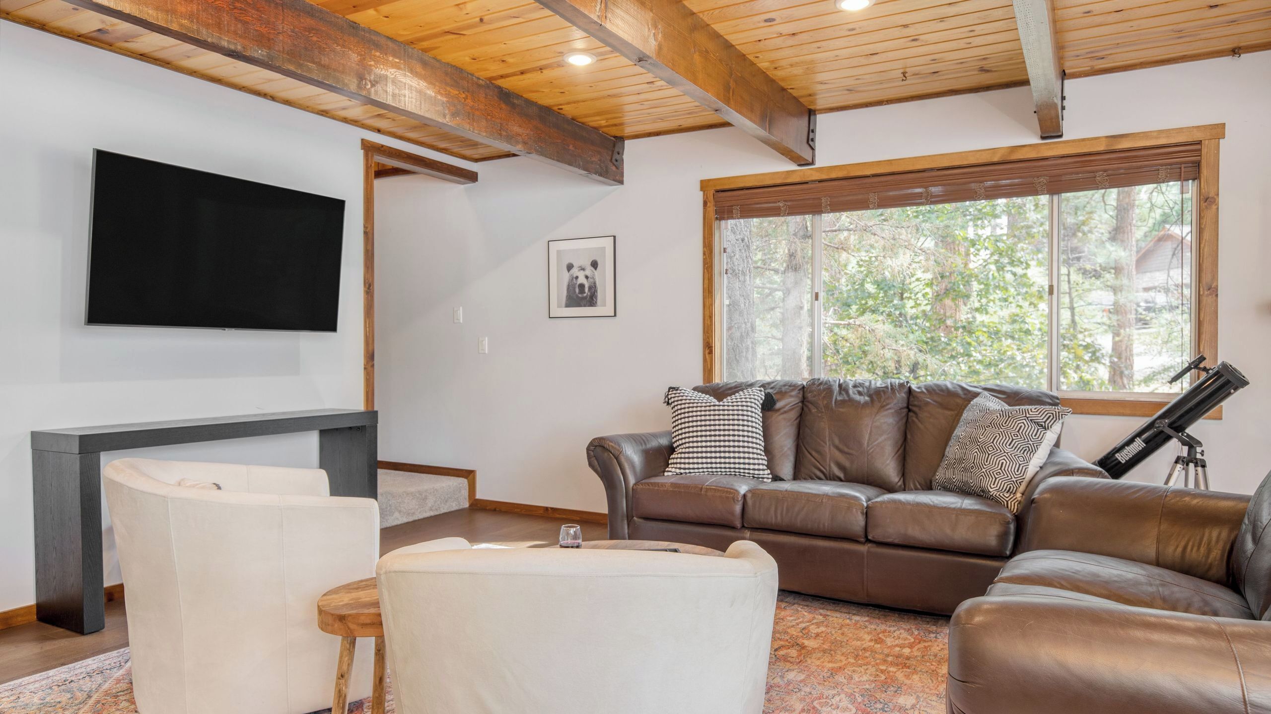 A living room with a brown leather sofa, a flat-screen TV, a fireplace, and a telescope.