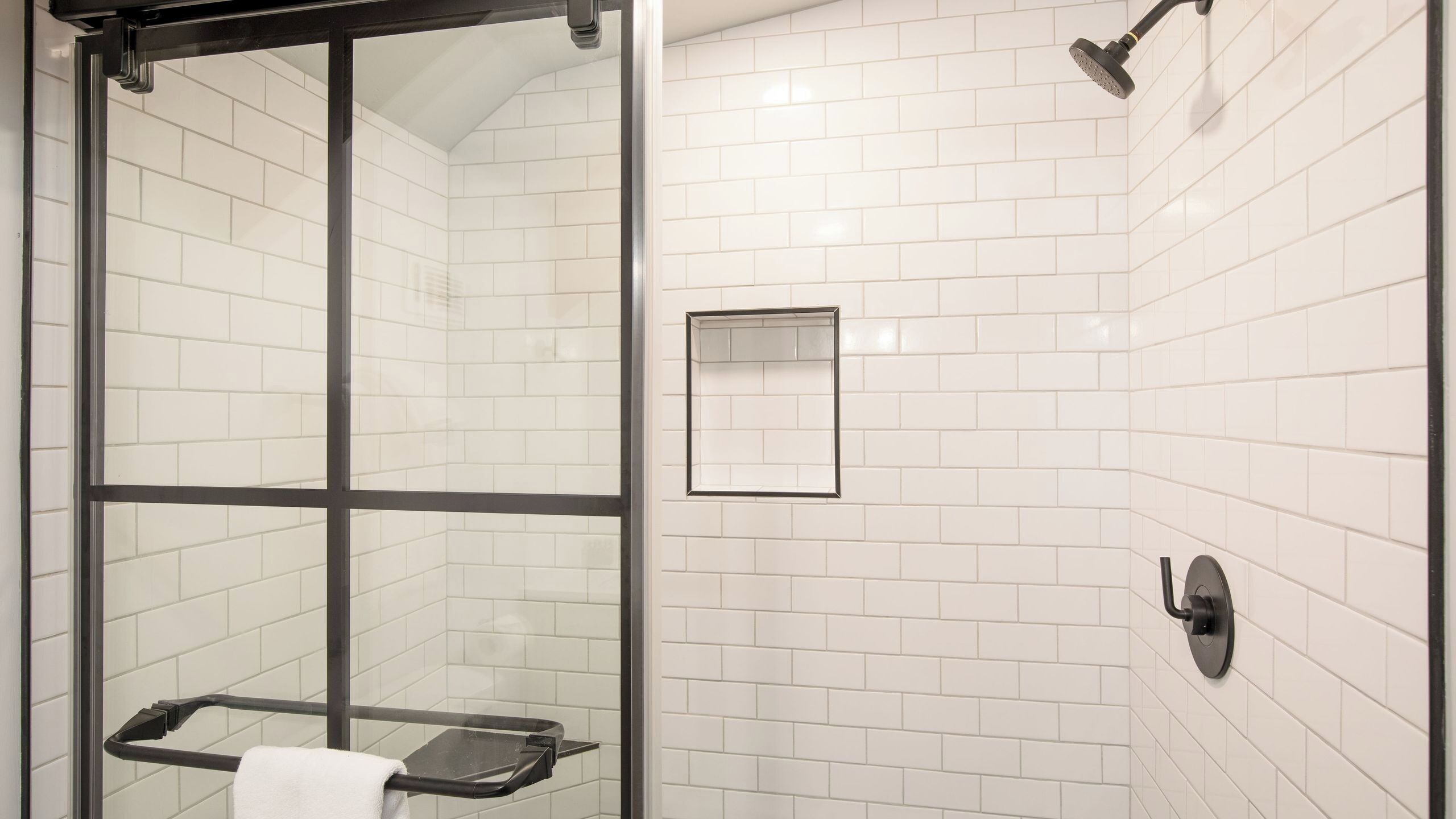 A glass-enclosed shower with a towel rack, a small mirror, and a showerhead.