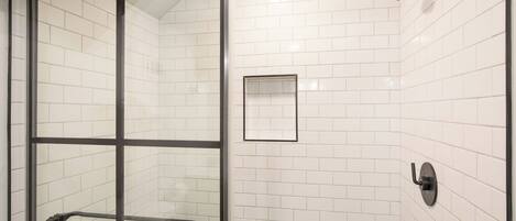 A glass-enclosed shower with a towel rack, a small mirror, and a showerhead.